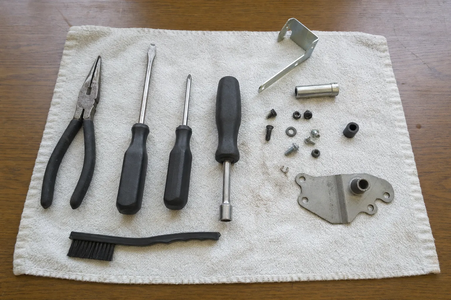 Needle-nose pliers, two screwdrivers and a nut driver with an angle bracket, a metal sleeve and a shaped mounting plate on a towel